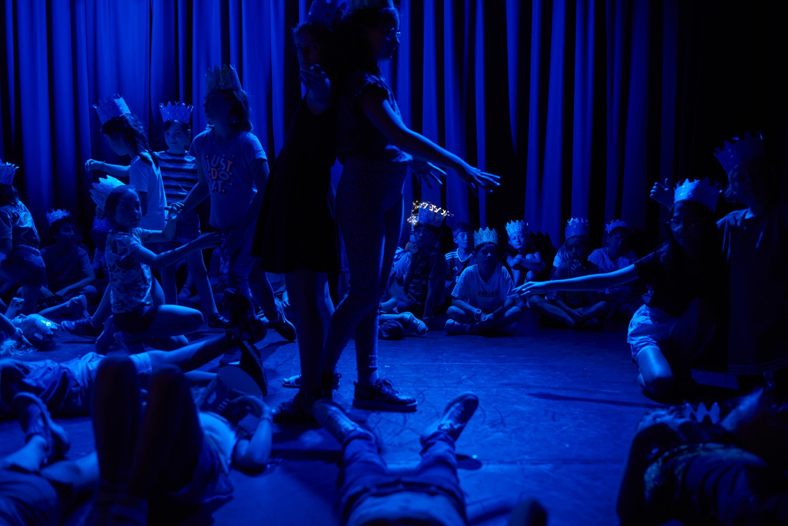 Spectacle avec une lumiere bleu des enfants sont assis et couché, deux enfants se tiennent debout